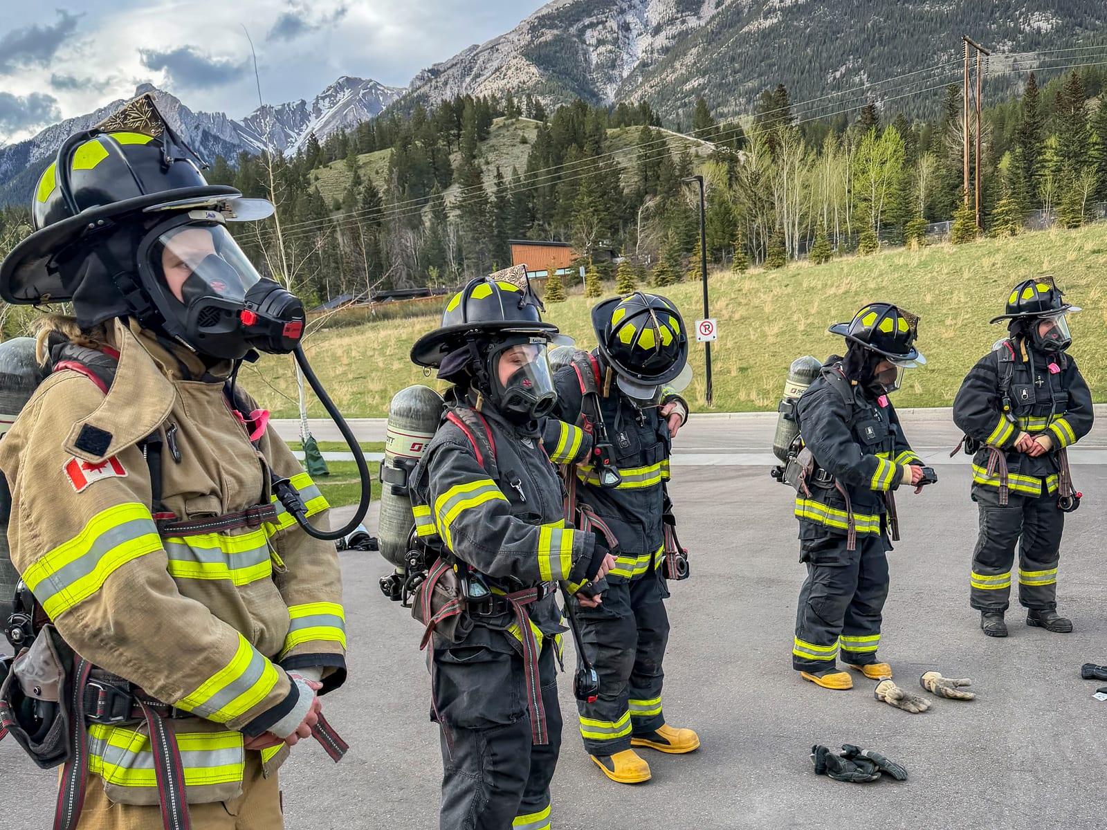 Firefighters in full turnout gear and breathing apparatus staged together before a training exercise, with mountains behind them.