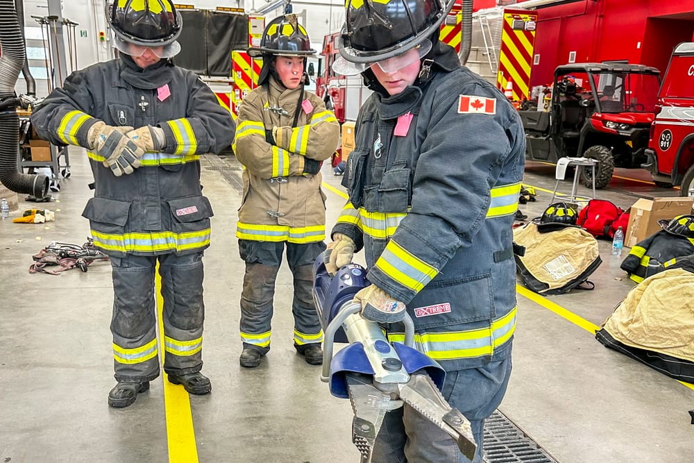 Firefighters handling hydraulic rescue tools inside an apparatus bay during practical training.