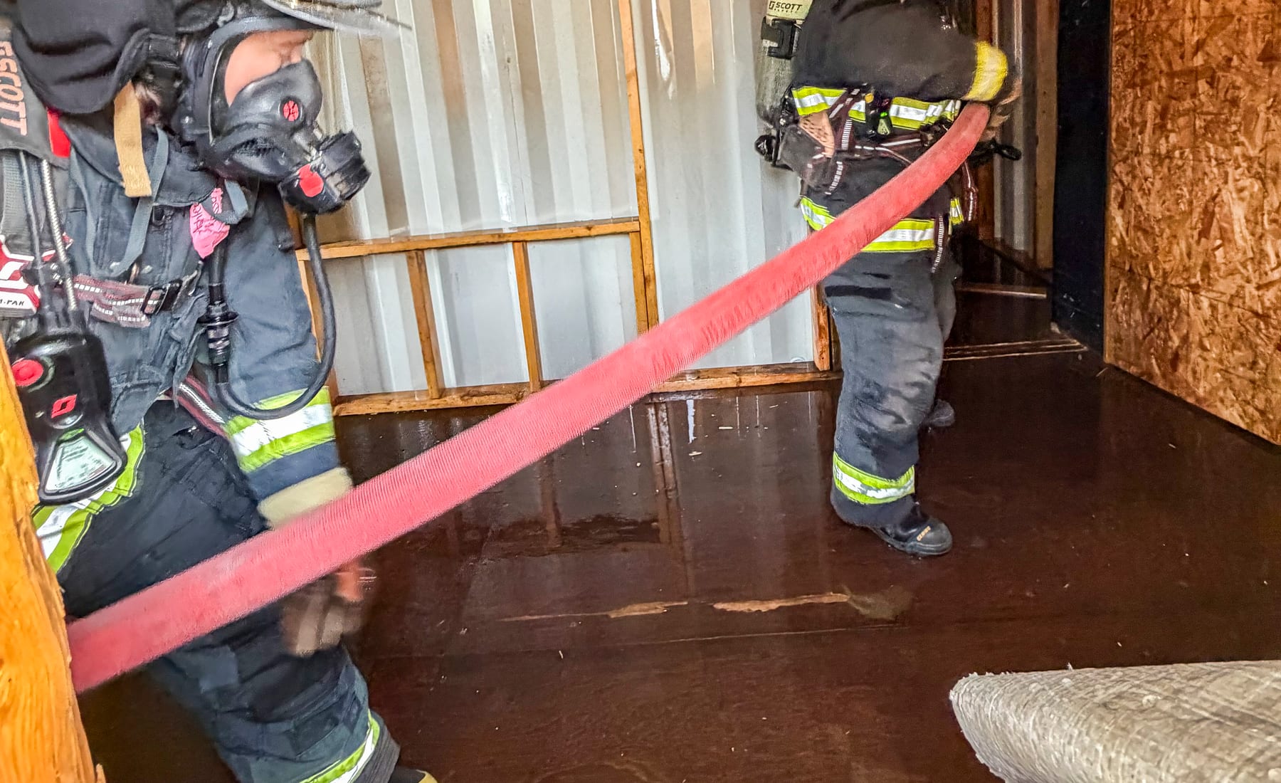 Firefighters in full turnout gear and breathing apparatus working a hose line during an interior attack training evolution.